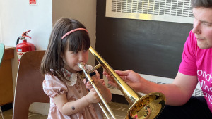 Child having a go at the trombone with the help of an LPO Foyle Future First
